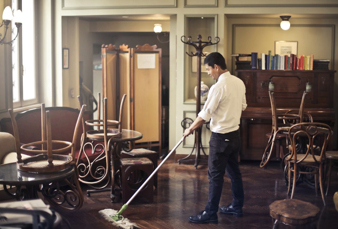 services-01 Side view of young ethnic male in uniform cleaning floor with mop while working in retro styled restaurant
